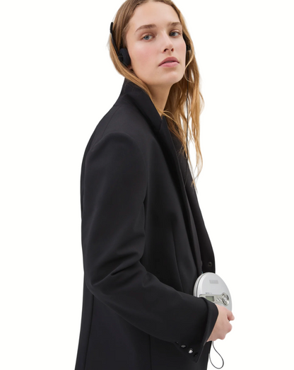 Woman wearing a black coat holding a white device on a plain background