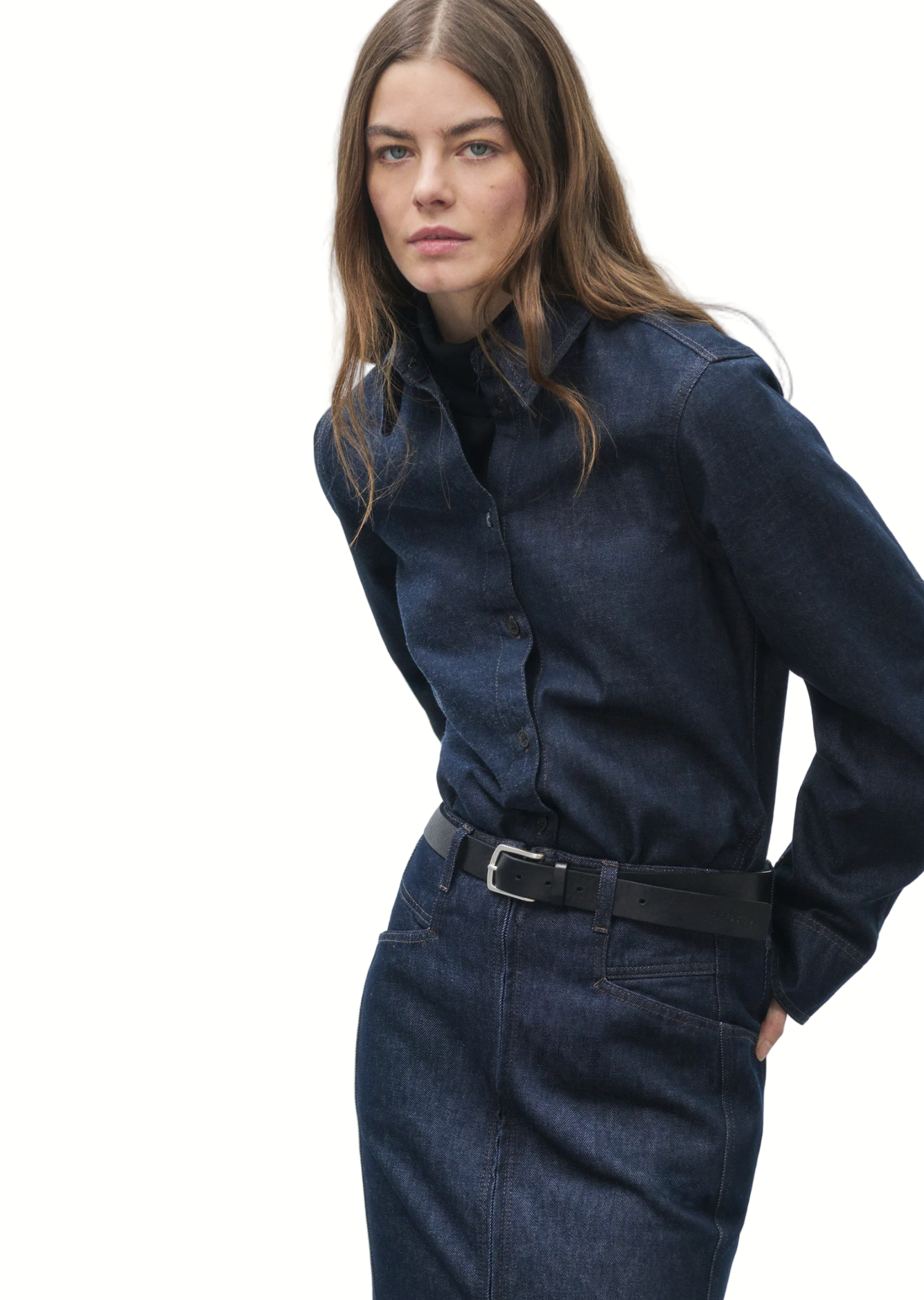 Woman wearing a dark denim shirt and jeans against a plain background