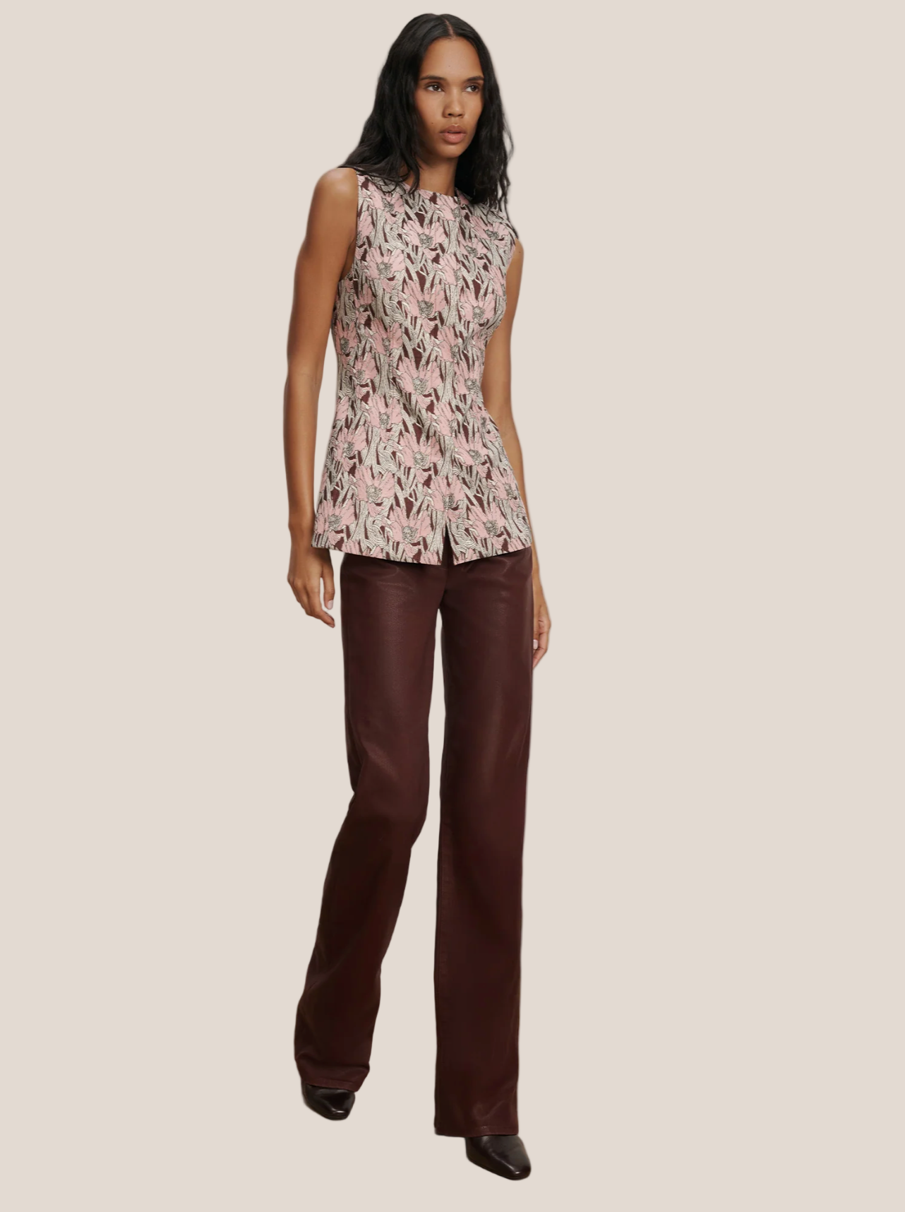 Woman wearing a patterned sleeveless top and brown pants on a plain background
