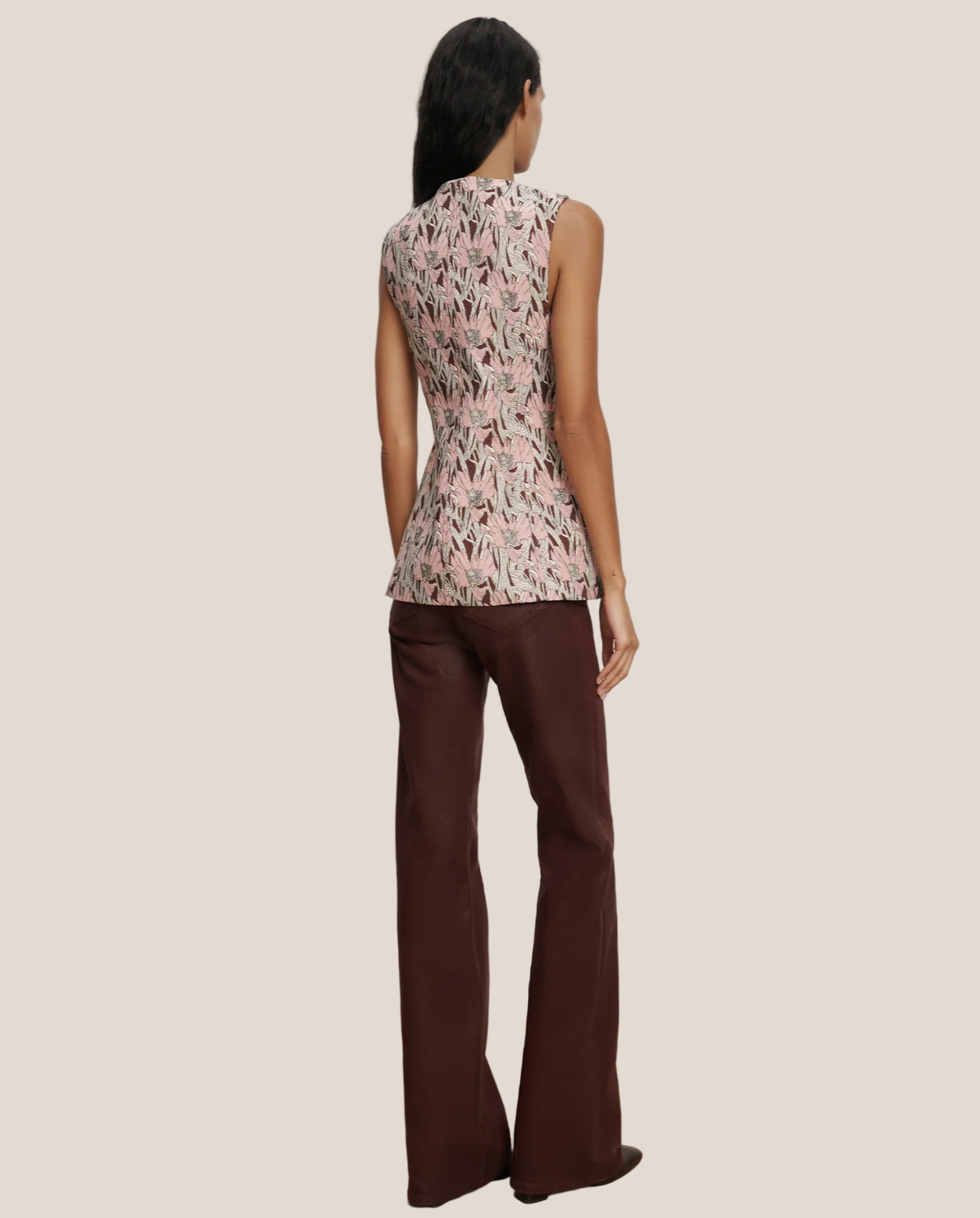 Woman wearing a sleeveless floral top and brown pants against a plain background