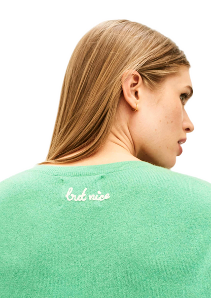Person wearing a green sweater with 'first nice' text on a light background