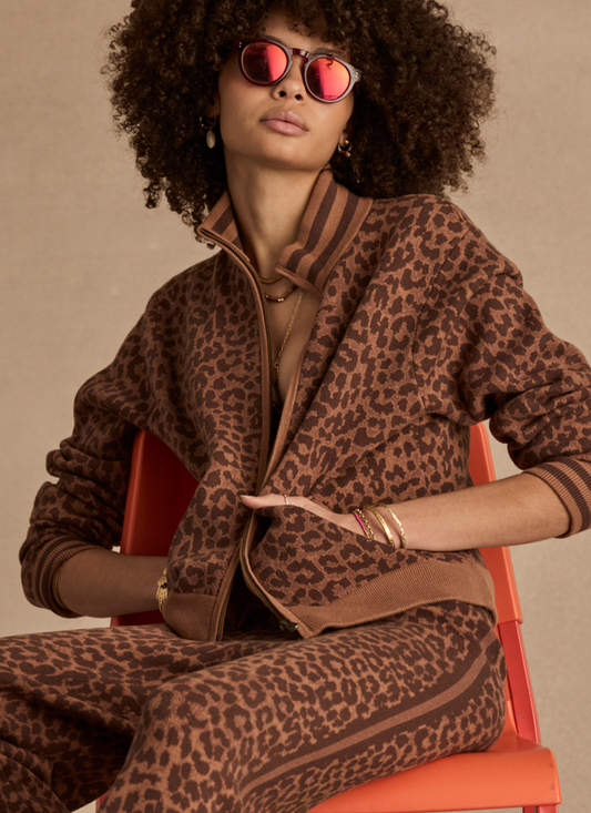 Woman wearing a leopard print outfit with sunglasses on an orange chair against a beige background