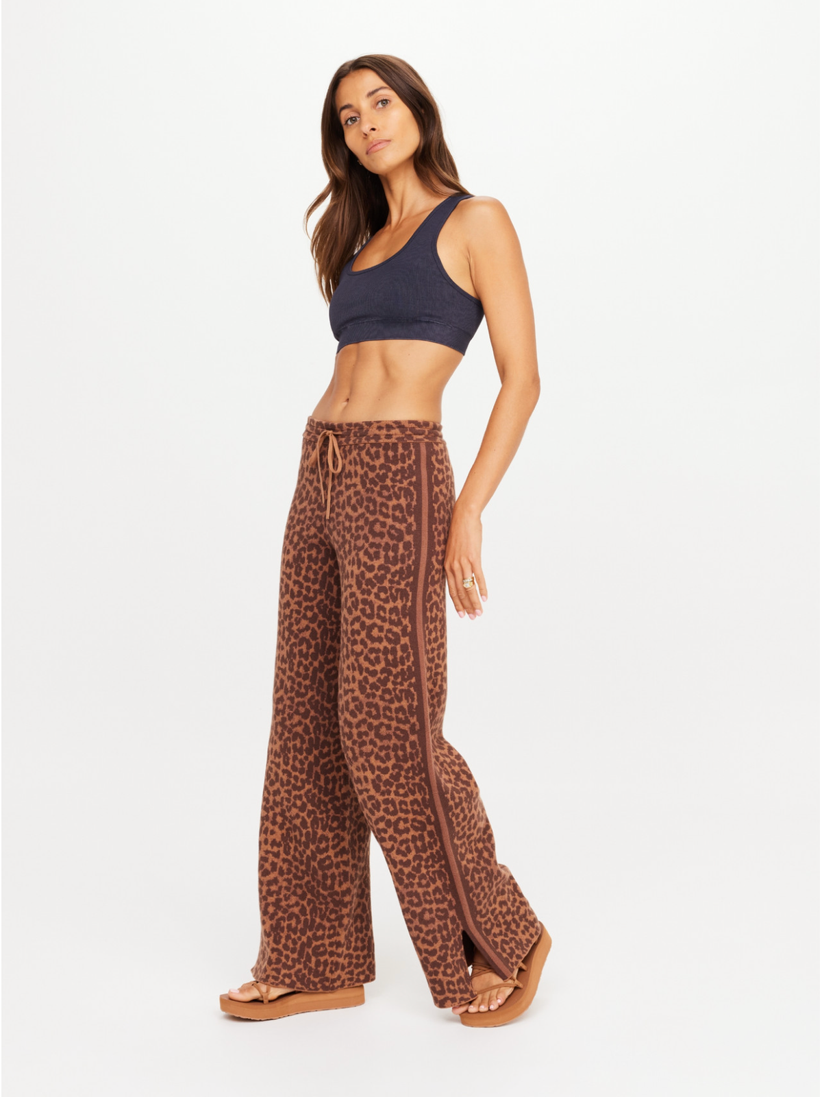 Woman wearing a leopard print pants and dark blue top on a white background