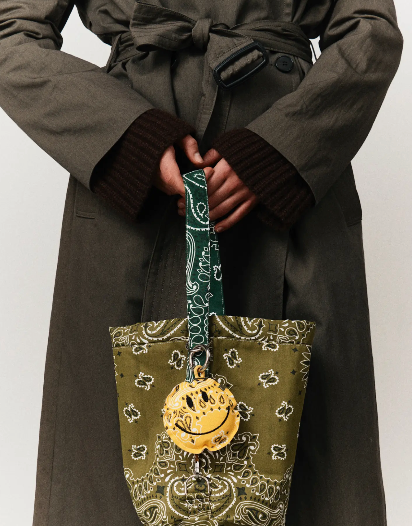 Person holding a patterned bag with a smiley face charm against a plain background