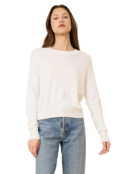 Woman wearing a white sweater and blue jeans against a beige background