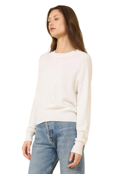 Woman wearing a white sweater and blue jeans against a beige background