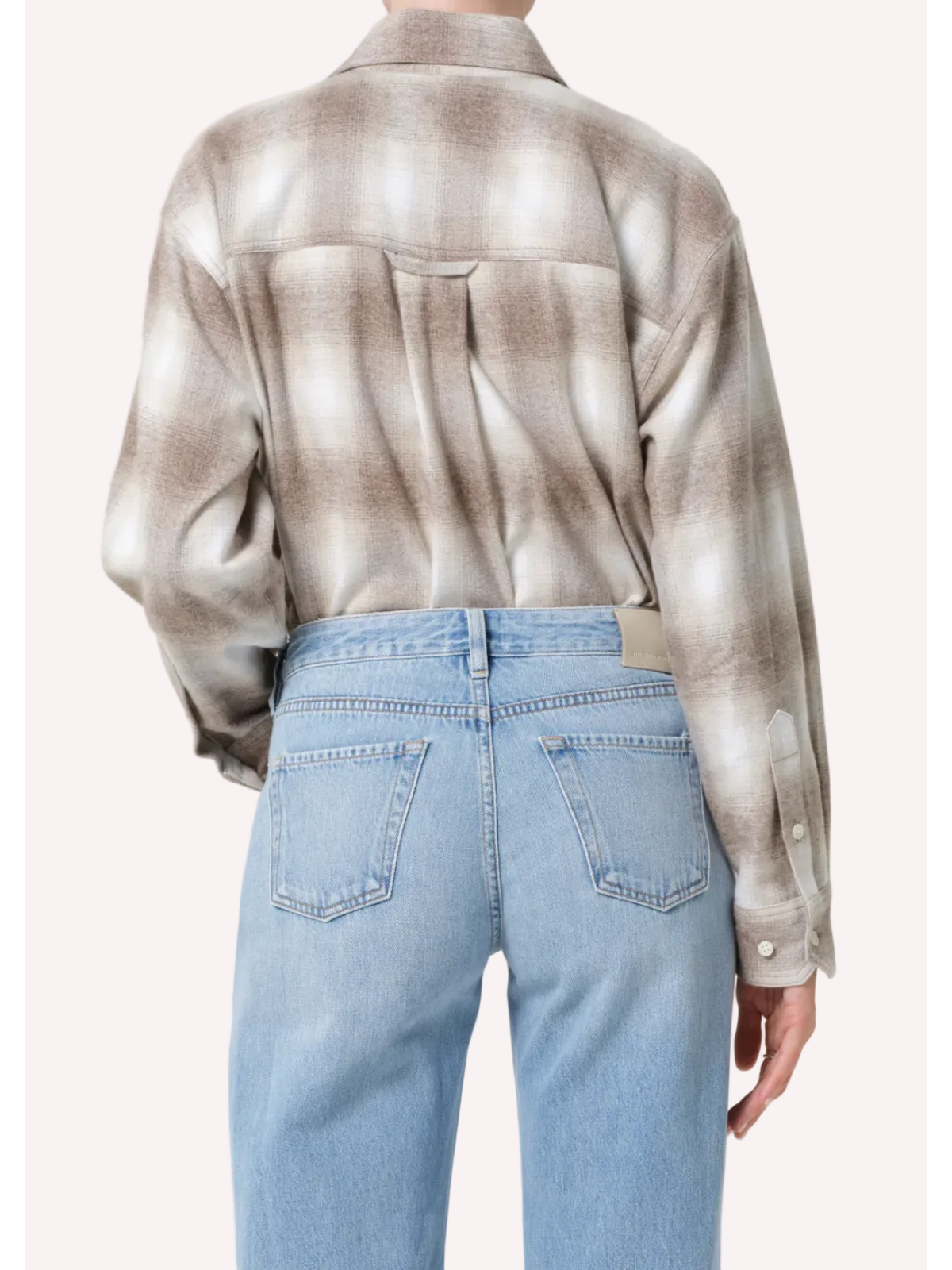Person wearing a patterned shirt and light blue jeans on a white background