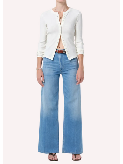 Person wearing a white cardigan and blue jeans on a plain background