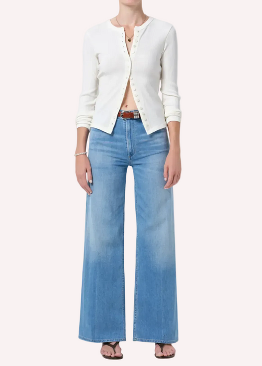 Person wearing a white cardigan and blue jeans on a plain background