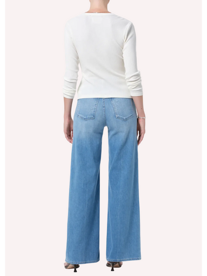 Person wearing a white long-sleeve shirt and light blue jeans on a plain background