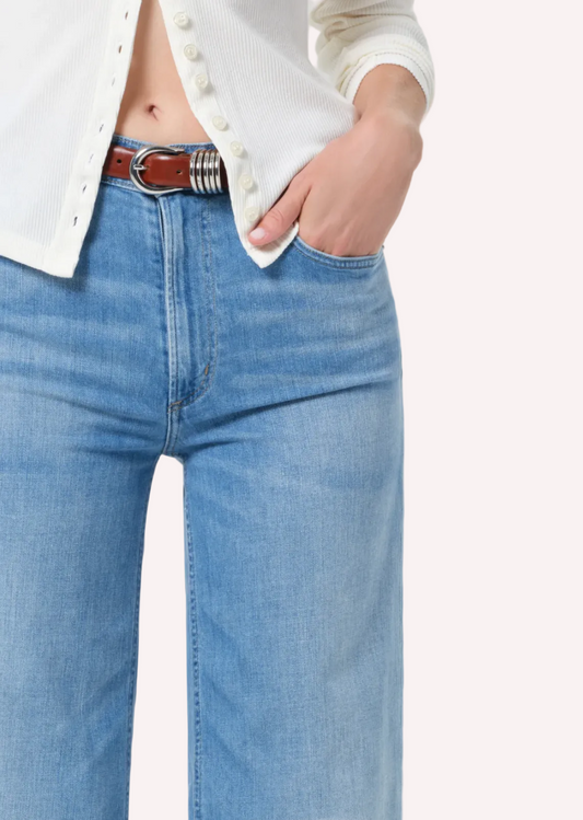 Person wearing blue jeans with a white shirt on a plain background